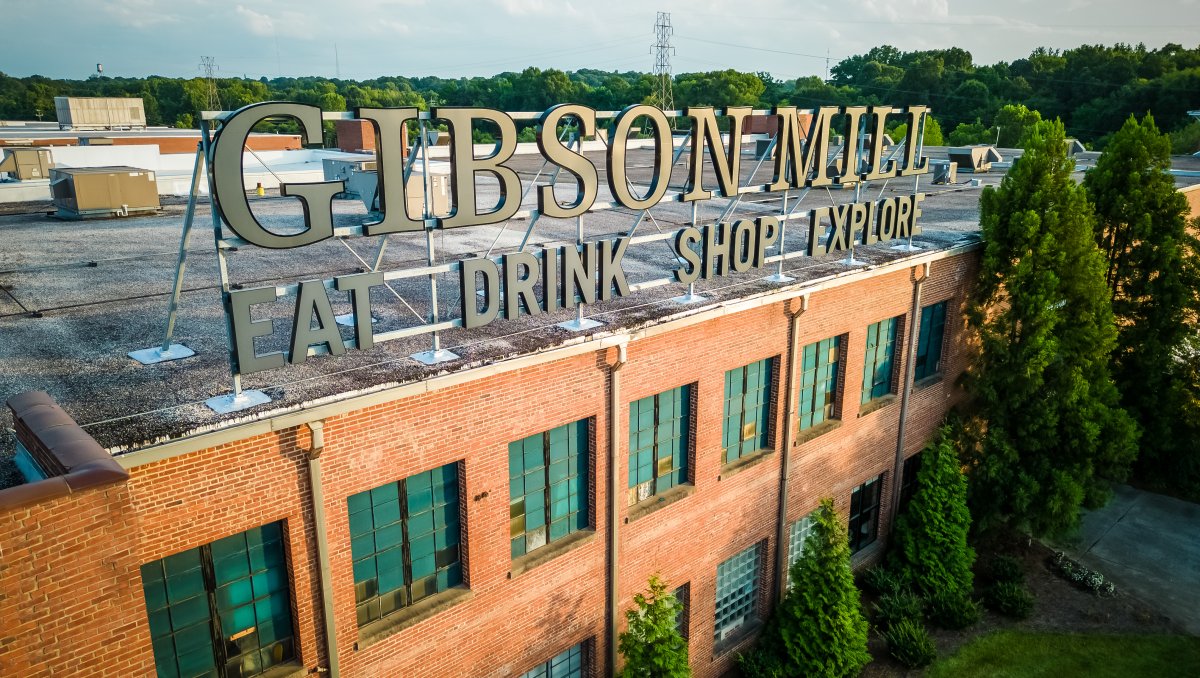 Exterior signage of Gibson Mill on top of brick building surrounded by trees.