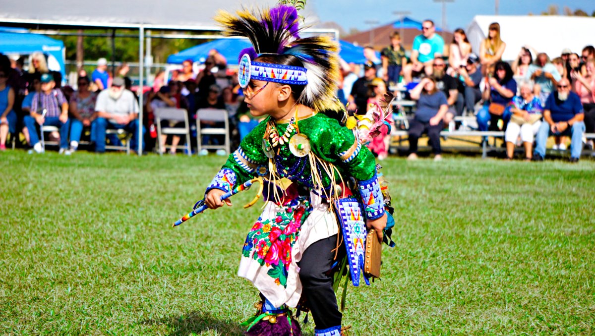 Native American child dancing in field with observers in background at Onslow Veterans Pow Wow