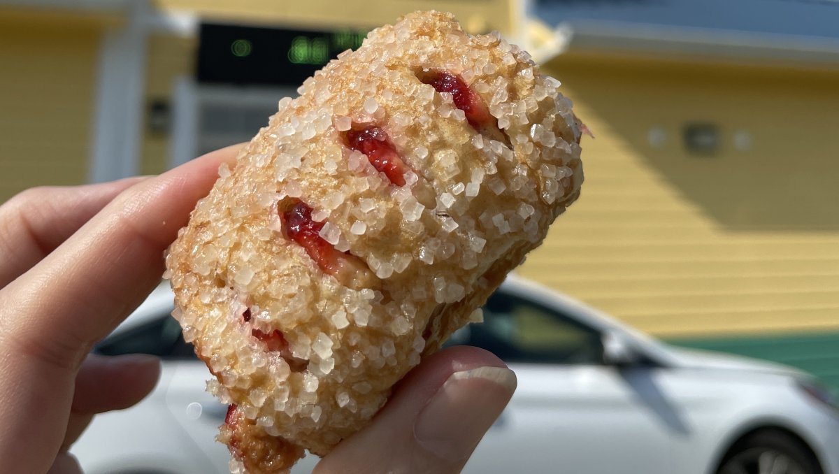 Person holding pastry in front of drive-thru awning of cafe