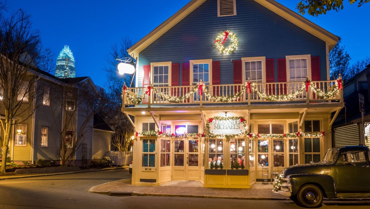 Exterior of blue restaurant with red shutters decorated for Christmas with Bank of America Building in background at dusk