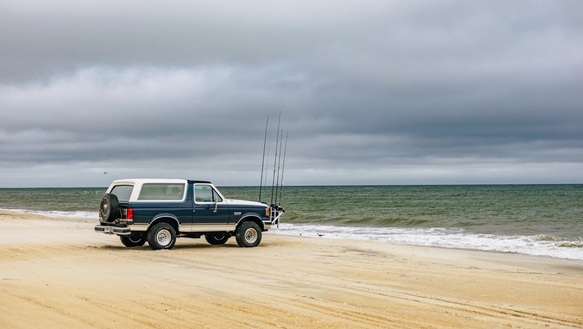 Ford Bronco along beach with cloudy, stormy skies over ocean.