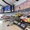 Museum exhibit of race cars and race trucks throughout the history of NASCAR, placed on a banking imitating a race track.