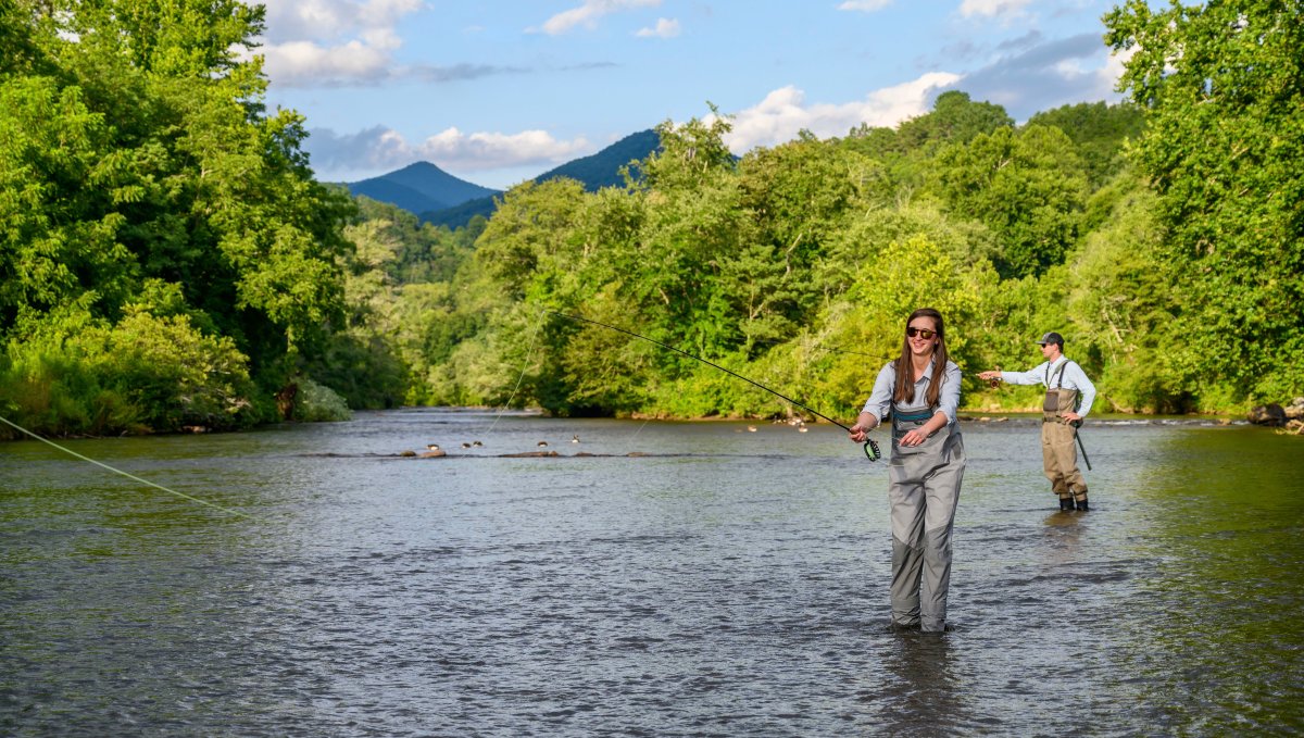 Two people fly-fishing in NC river with mountains in distance.