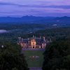 Aerial of Biltmore House and grounds at dusk with Blue Ridge Mountains in background under purple sky.