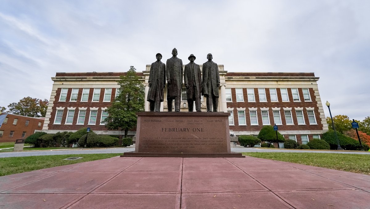 Worm's-eye view of February One Monument in front of brick Dudley Building on campus.