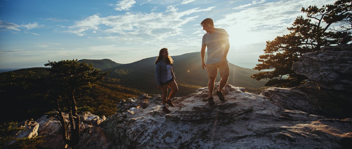 Couple hiking on Hanging Rock Trail in Hanging Rock State Park with mountains in distance and sun in distance