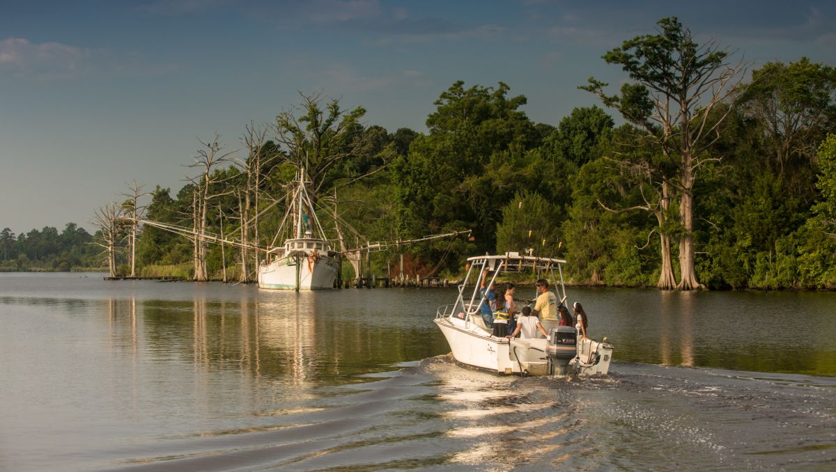 Group of people on fishing boat on river with a boat, trees and land in distance