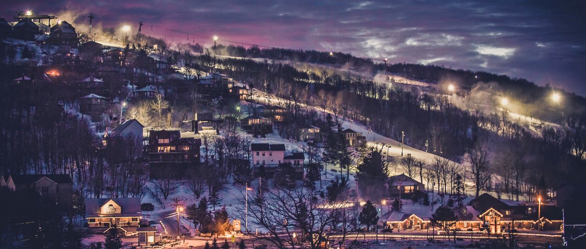 Longrange view of ski slopes and community at night, lit up under dark blue sky