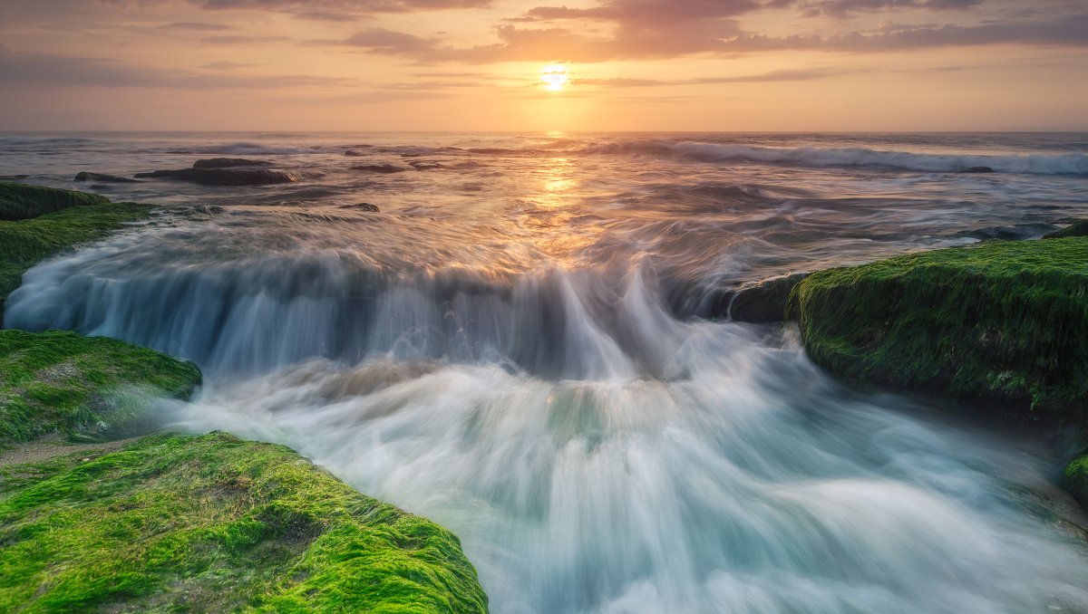 Ocean water rushing over Coquina Rocks with sun over water in distance