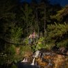 Two people on suspension bridge crossing over river at night on zip line tour.