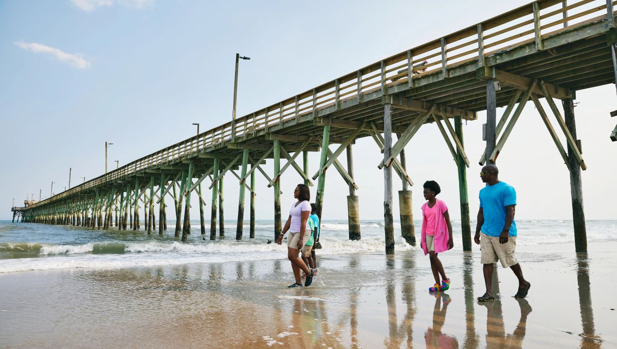 Family walking on beach in front of pier jutting out into ocean