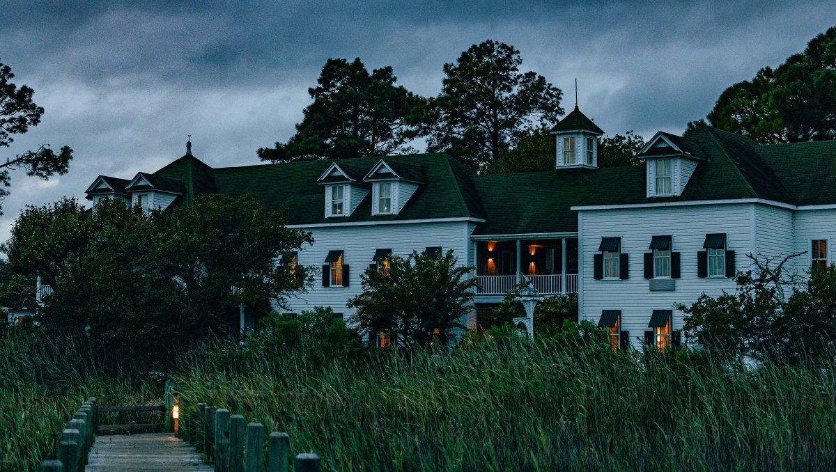 Exterior of white coastal inn at dusk with room lights lit and sea oats in foreground