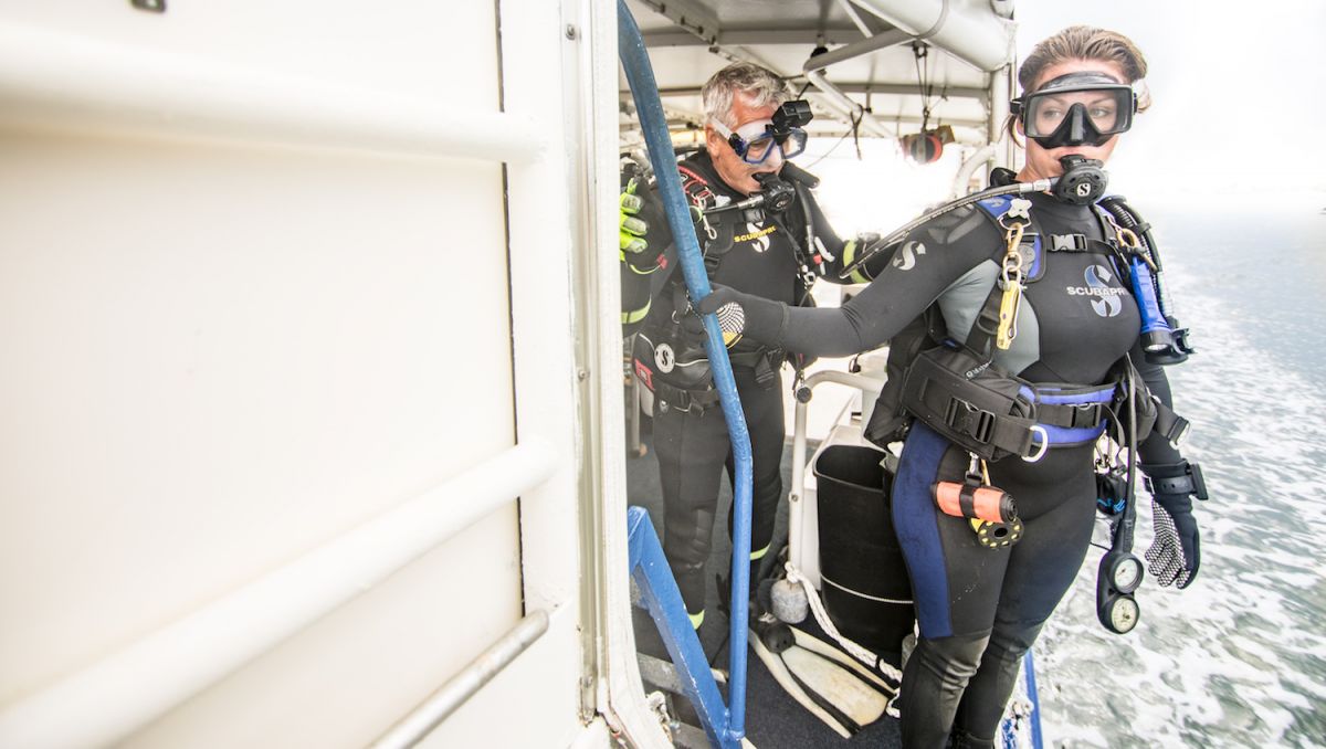Woman in full Scuba gear preparing to jump off boat with man in full gear behind her