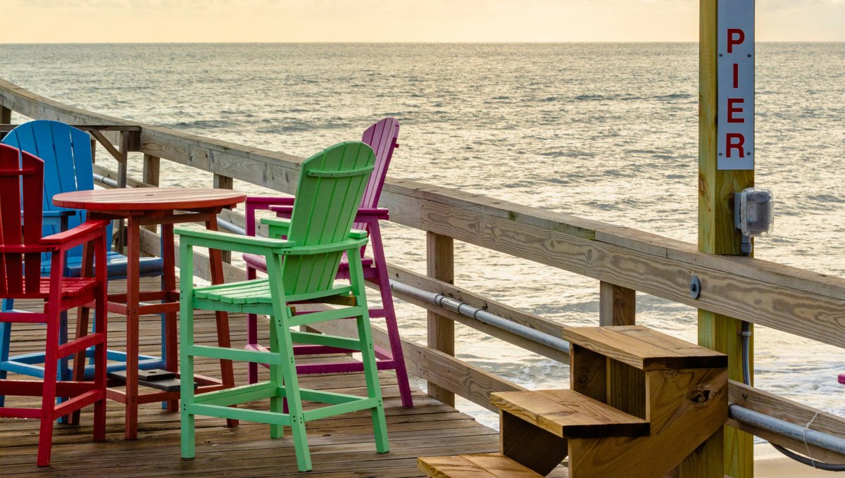 Colorful table and chairs sitting on pier with Nags Head Fishing Pier signage on wood stand