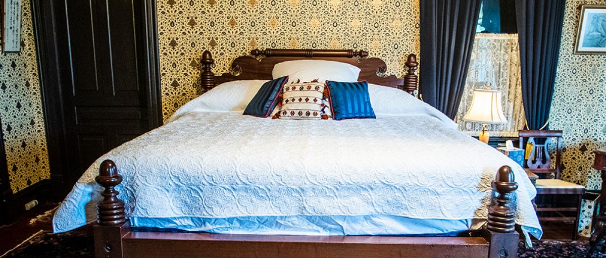 Antique-looking bedroom in the Music House with red carpet, navy blue blinds and gold wallpaper 