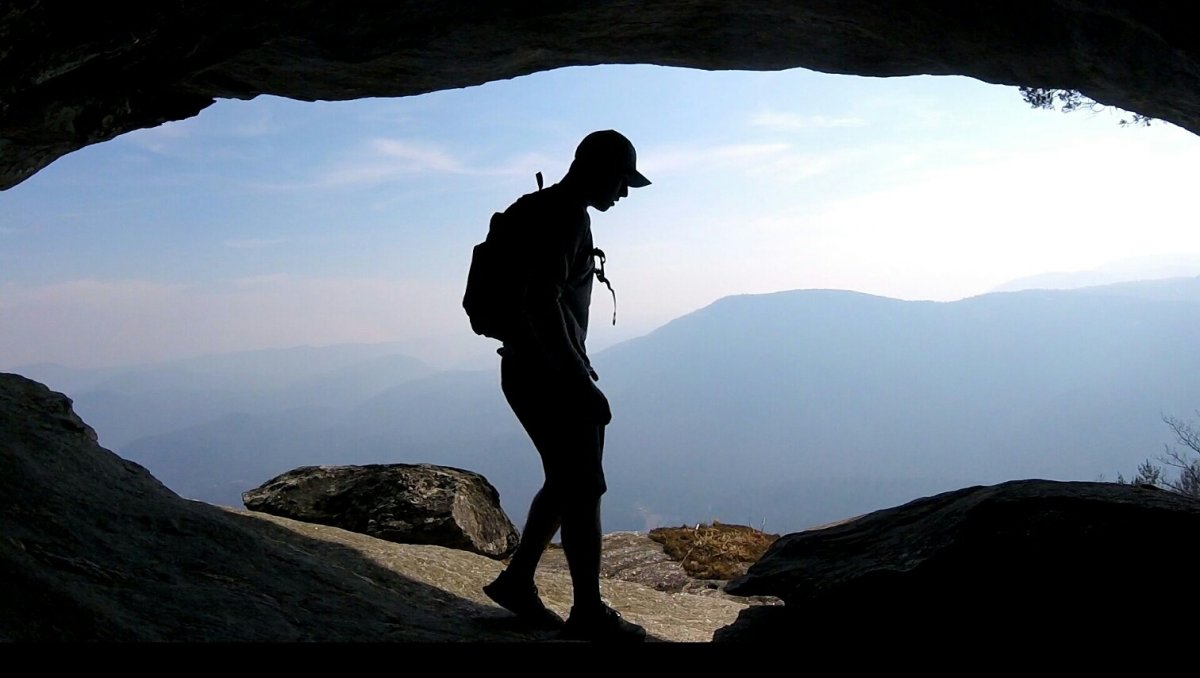 Silhouette of hiker in mouth of cave with mountains in background.