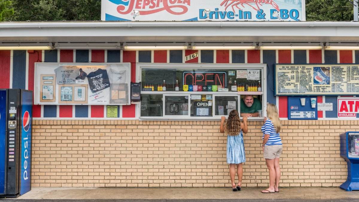 Mom and daughter ordering food at window of old-timey-looking brick food stand