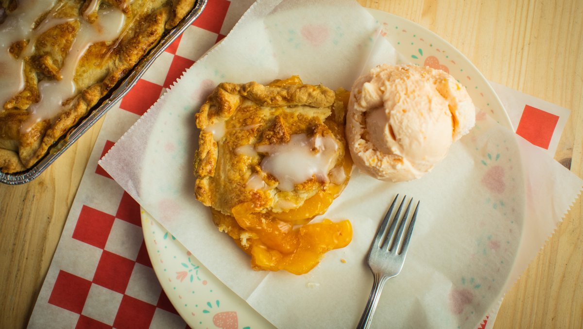 Aerial, closeup view of peach sonker and scoop of vanilla ice cream on plate with tray of sonker beside it