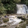 Person sitting on rocks admiring Yellow Creek Falls and surrounded by trees.