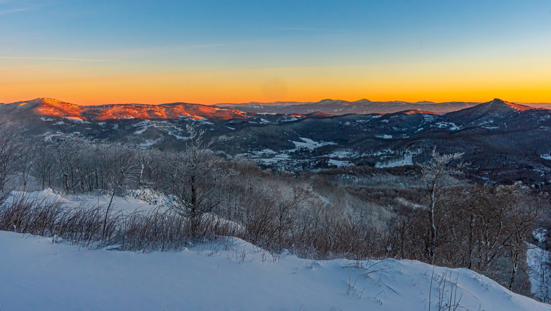 Sunrise over mountain range with snowy trees in foreground.