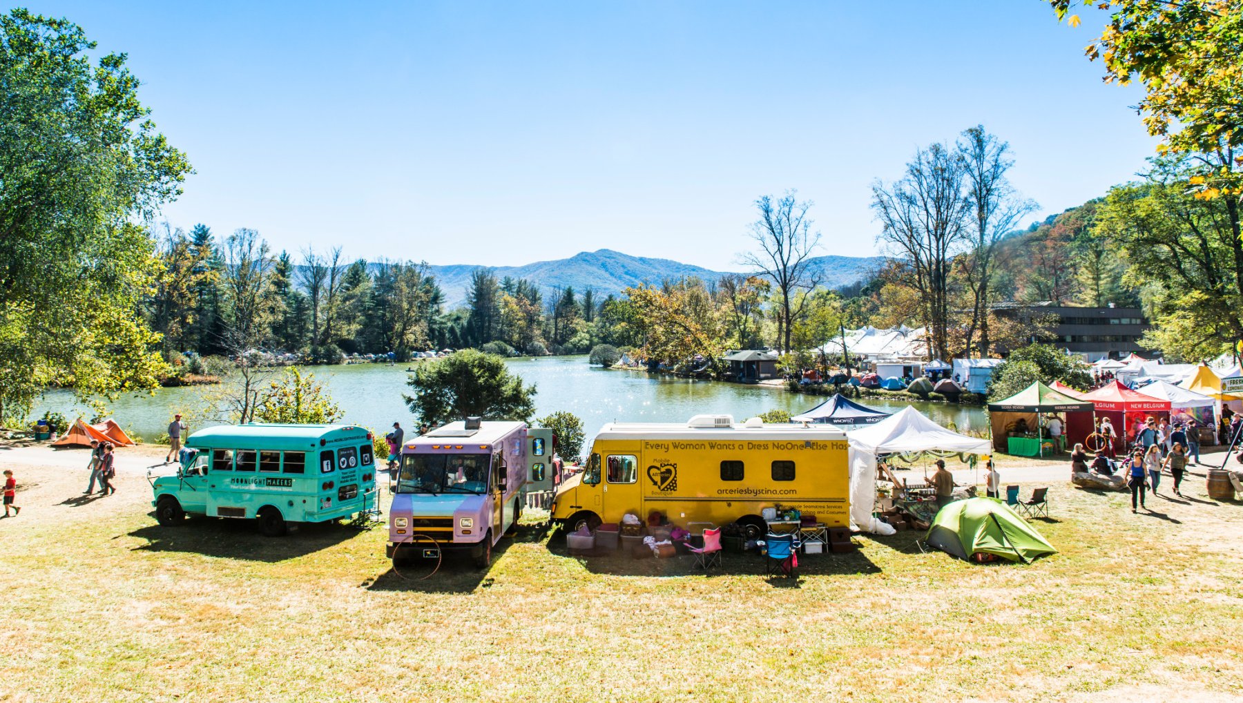 Colorful food trucks and festival vendors set up around lake with fall foliage and mountains in background