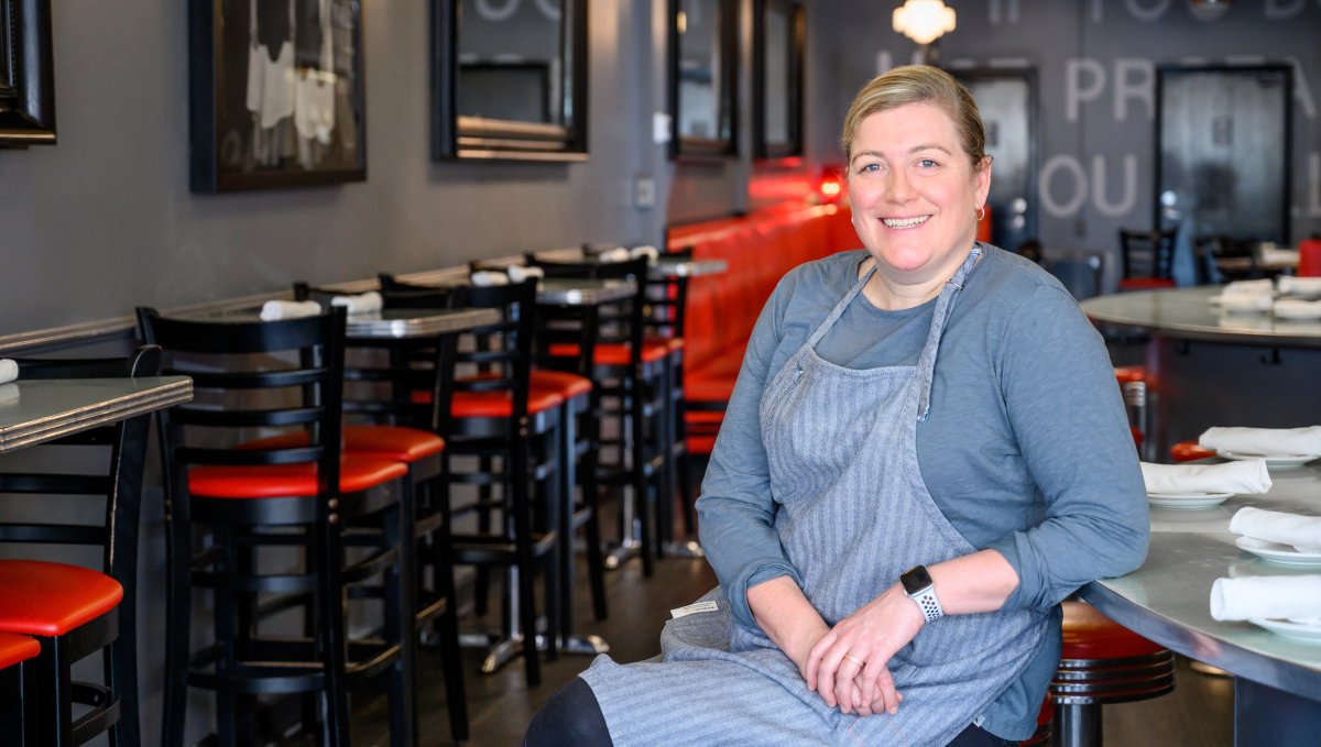Chef Ashley Christensen sits at table smiling at camera in her restaurant Poole's Diner.