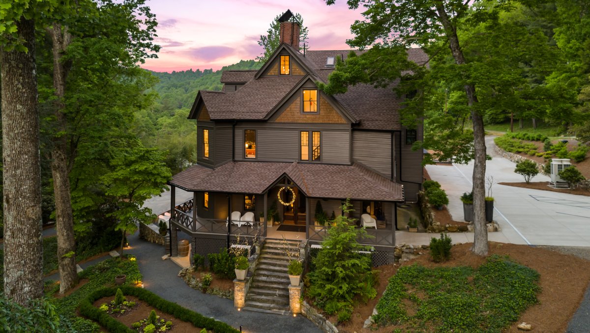 Aerial of restored mountain inn surrounded by green grounds and mountains views in background.