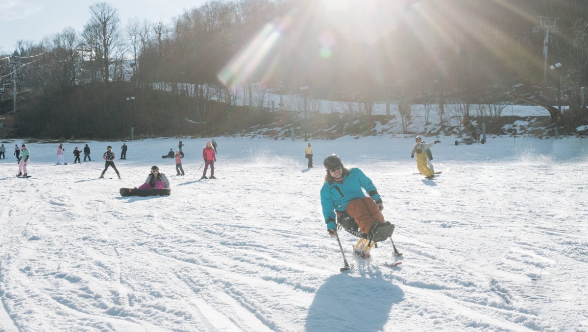 Person riding down mountain on adaptable skis with people on slope in background