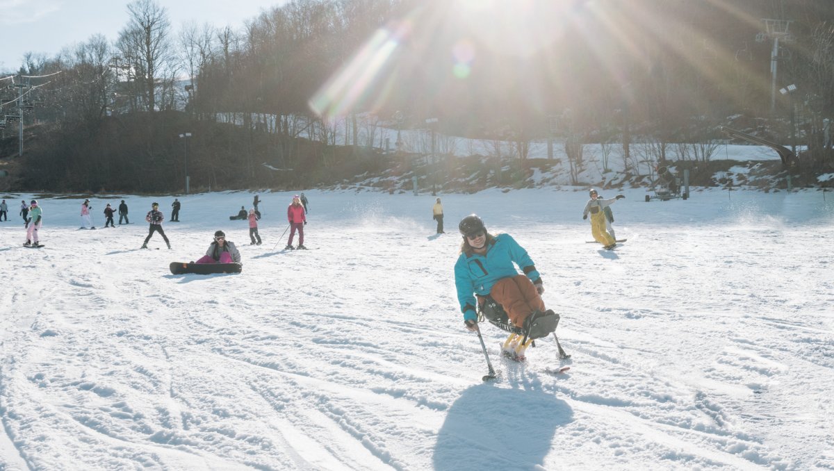 Person riding down mountain on adaptable skis with people on slope in background