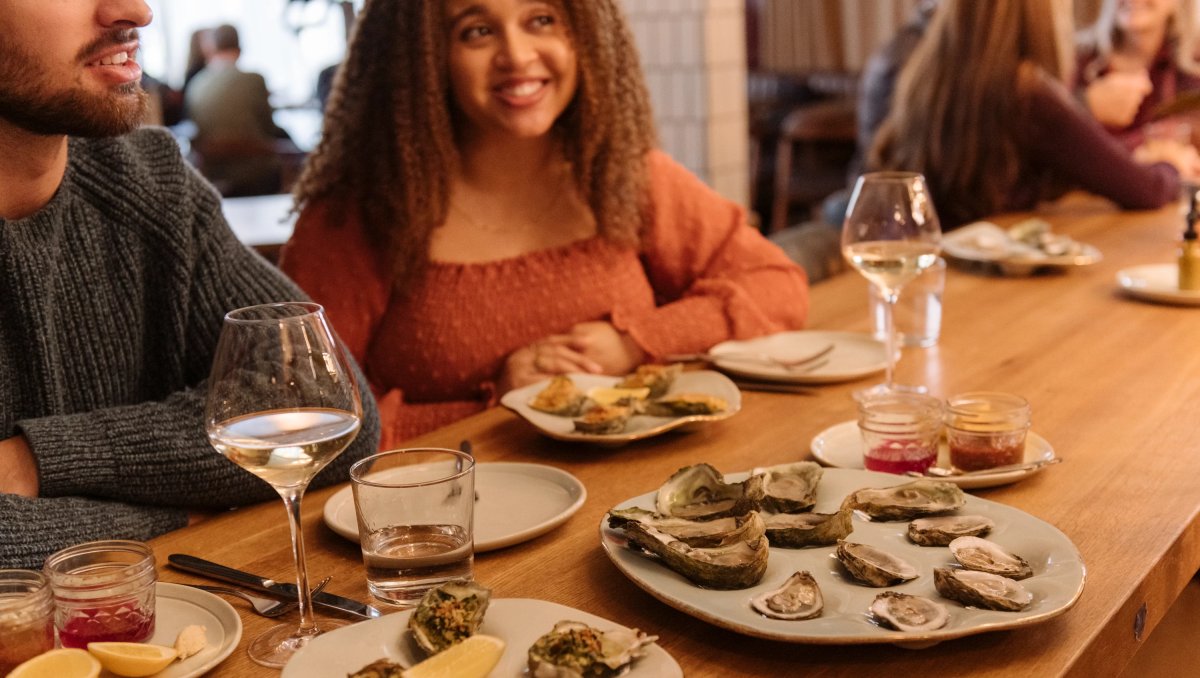 Couple sitting at bar with plates of oysters and wine in front of them