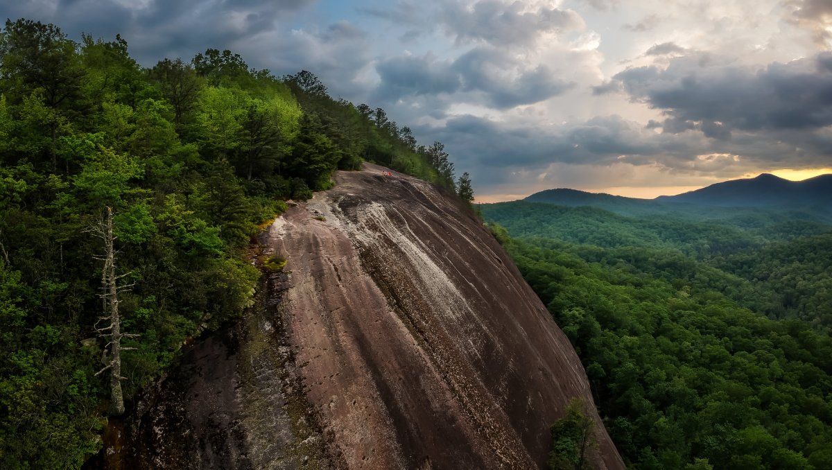 Huge mountain rock with green trees on it surrounded by other green mountains