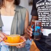 Two people holding coffee with Cocoa Cinnamon decal on cups.