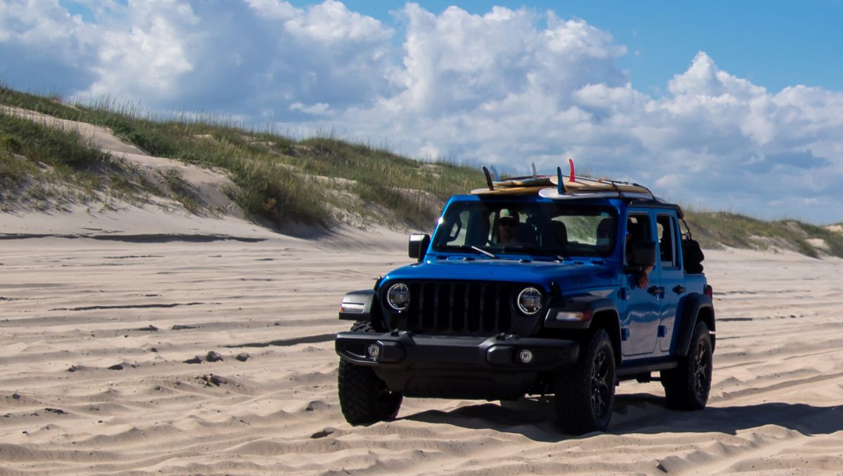 Blue 4x4 vehicle driving on sand parallel to dunes