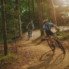 Two people cycling on Cub Creek Mountain Bike Trails with sun streaming through trees in forest