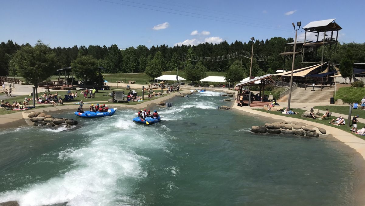 Whitewater rafters on water at U.S. National Whitewater Center with people watching from land on sunny day