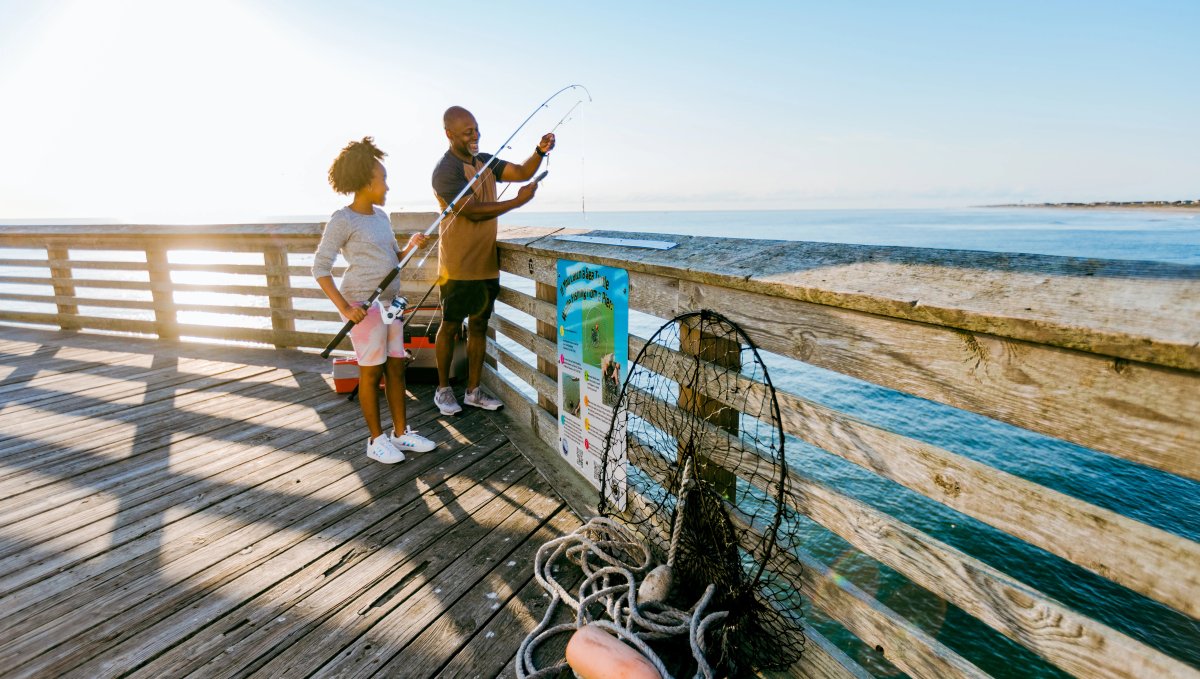 Father taking fish off daughter's fishing line while fishing off an ocean pier
