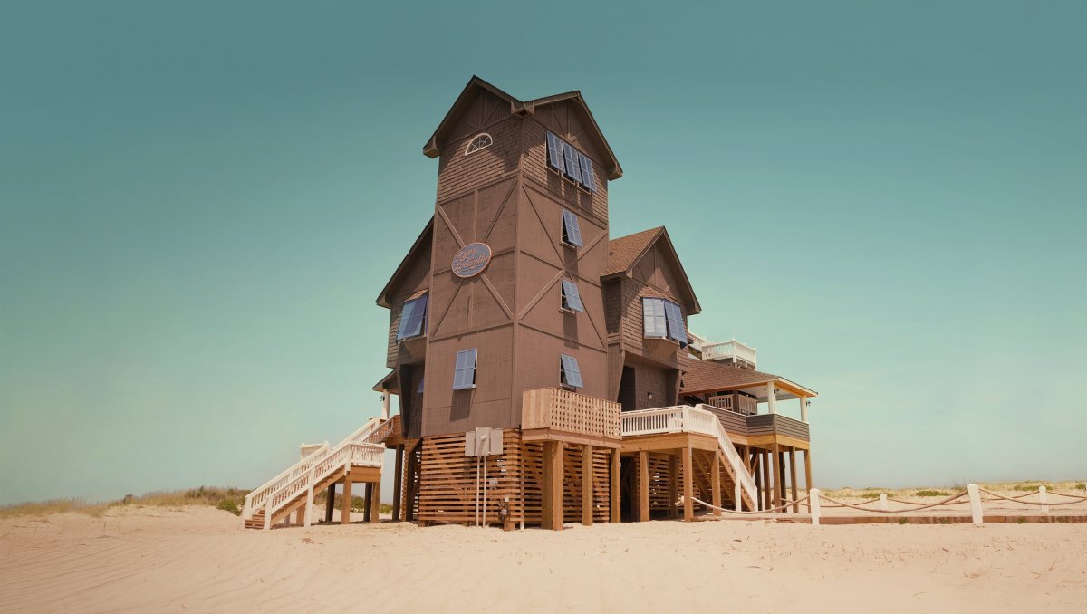 Large beach house standing alone surrounded by sand during daytime
