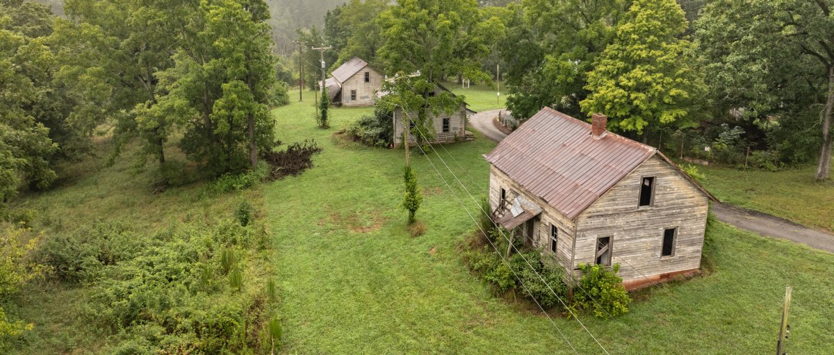 Aerial of of three cabins at Henry River Mill village surrounded by green trees.