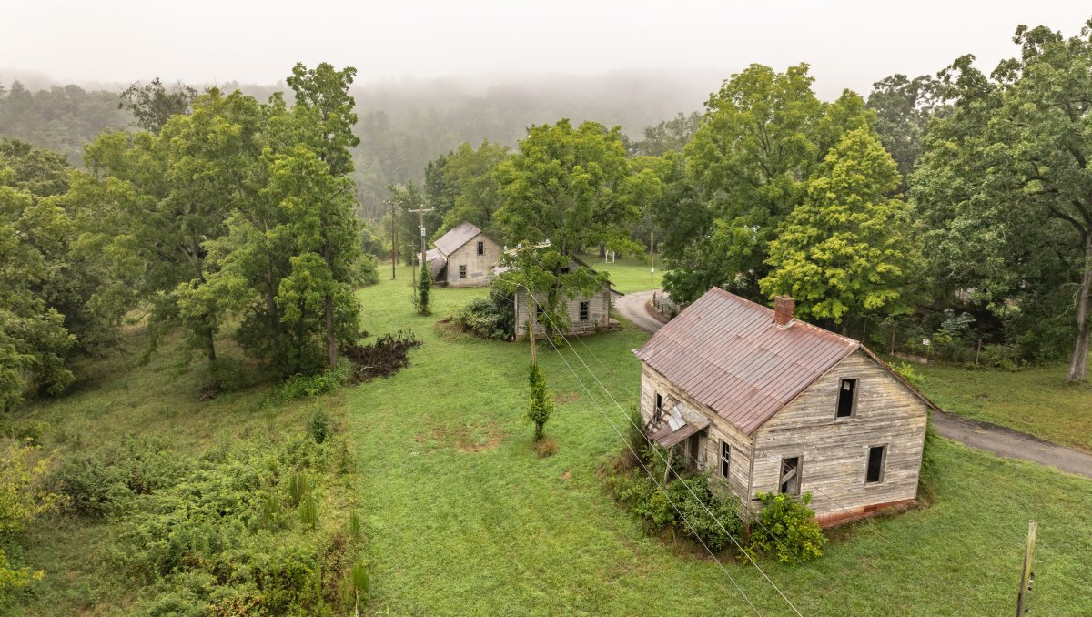 Aerial of of three cabins at Henry River Mill village surrounded by green trees.