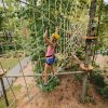 Child on aerial ropes course among trees during daytime.