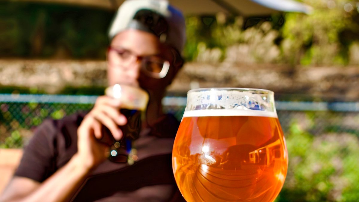 Person drinking beer at picnic table with full beer on table in foreground