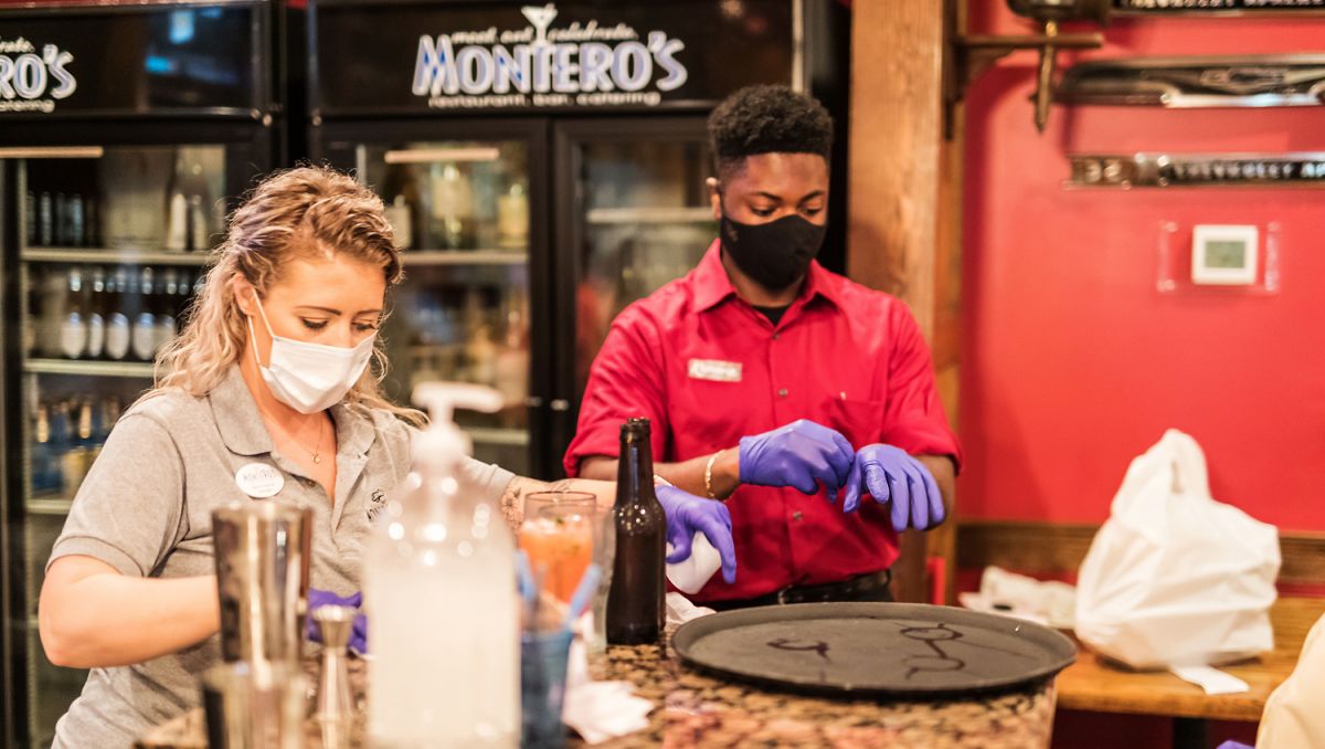 Two employees wearing masks at Montero's Restaurant putting on gloves while standing at bar