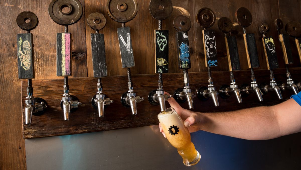 Hand coming from outside frame to pour a beer from a wall of taps