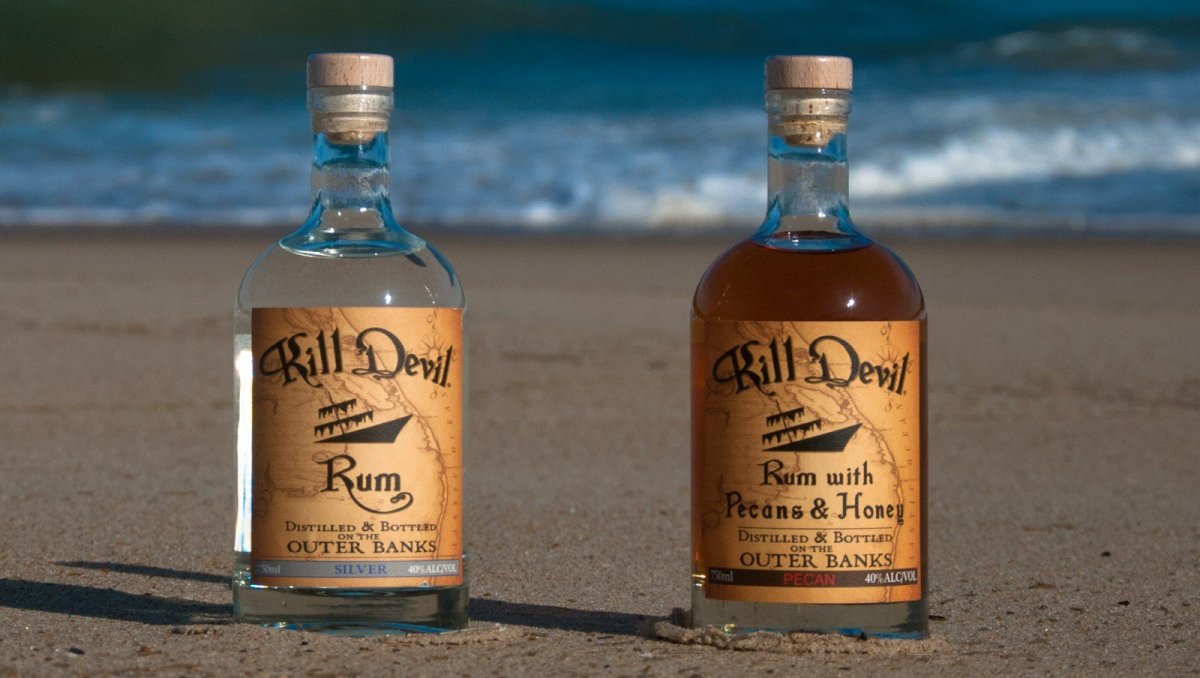 Two bottles of Outer Banks Distilling's Kill Devil Rum on sand with waves rolling in background