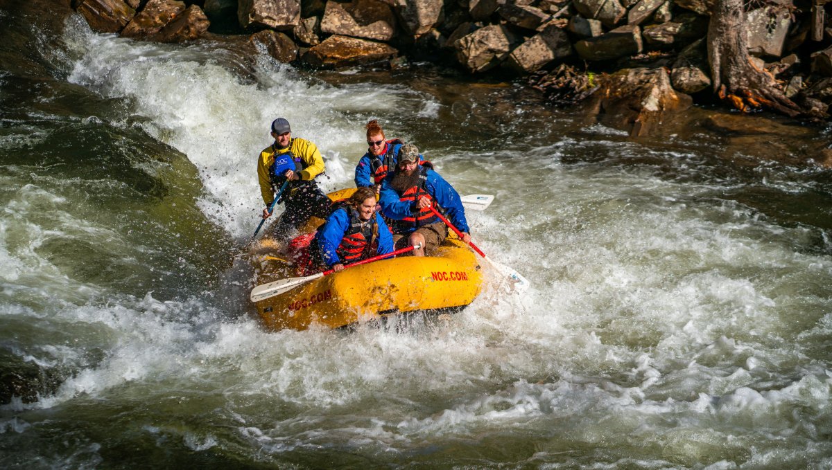 Four people on raft going down whitewaters with rocks in background