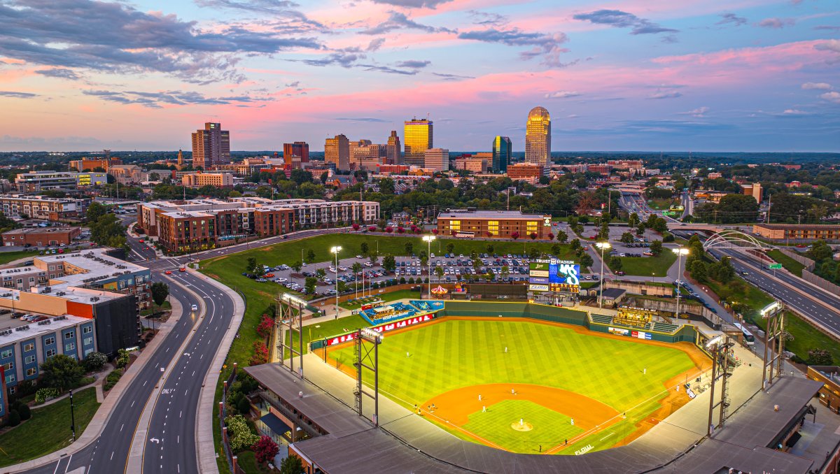 Aerial view of Winston-Salem Dash stadium, Truist Stadium, with road to the left and skyline in background at dusk under pink and blue sky