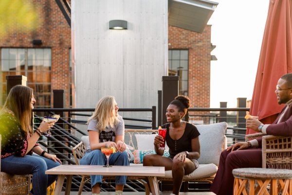 Four friends enjoying drinks on rooftop during daytime