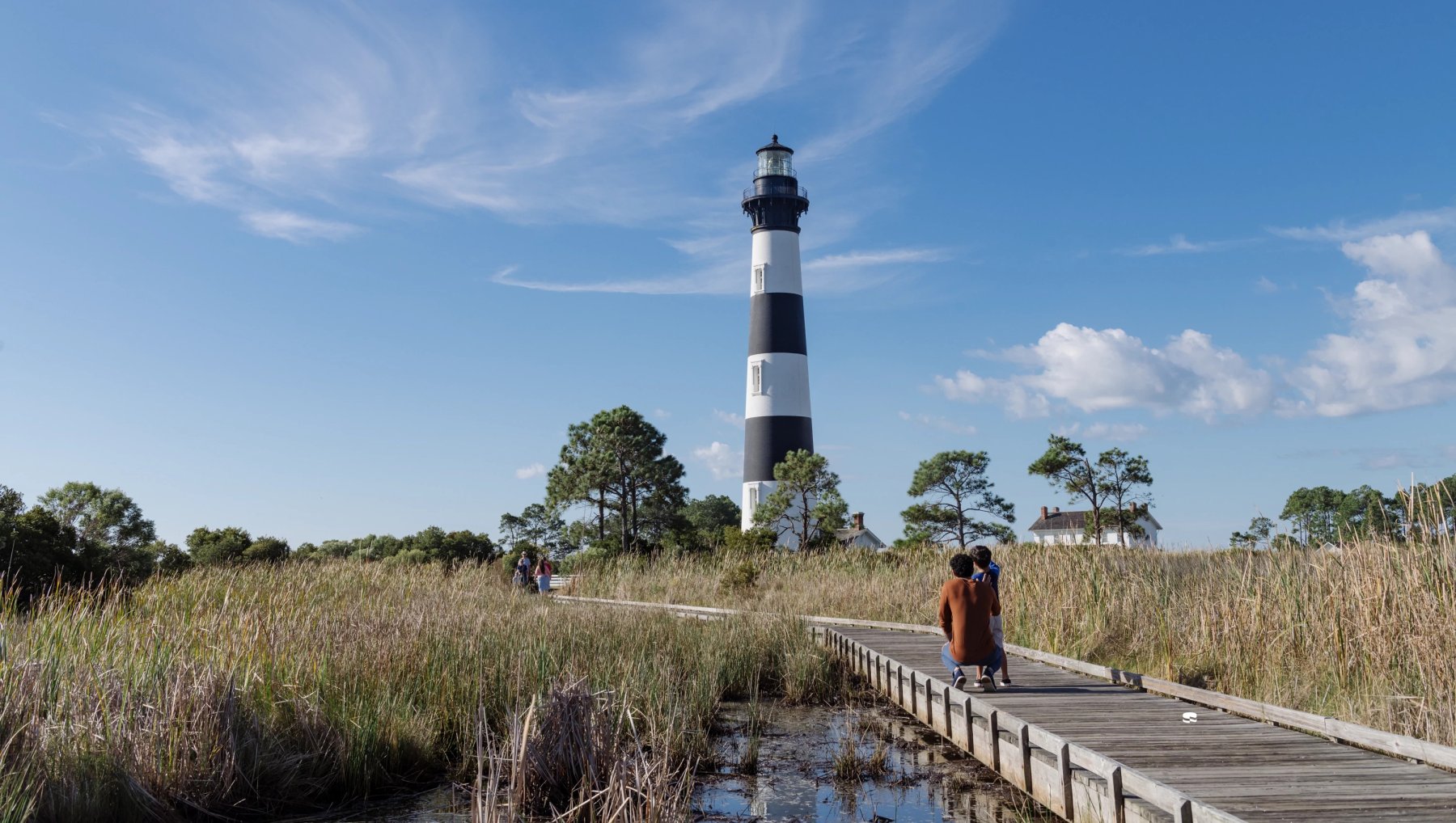 Father and son on pathway through marsh looking up to admire Bodie Island Lighthouse in fall.
