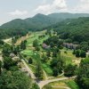 Aerial of golf course, condos and trees in front of tree-lined mountains during daytime