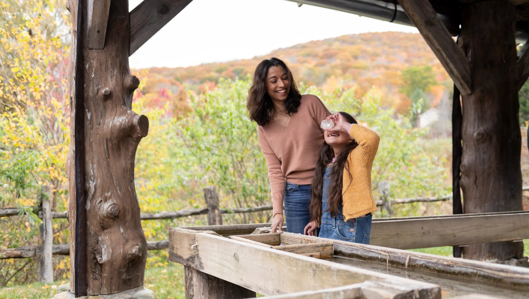Mother and daughter finding gems in Sugar Creek Gem Mine with fall foliage in background.